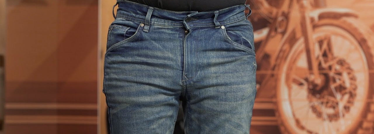 Person wearing blue Bull-it jeans with a blurred background featuring a motorcycle.