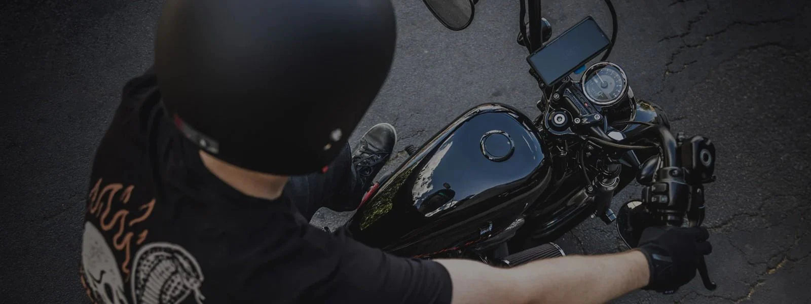 Person wearing a helmet and gloves sitting on a motorcycle with a Quad Lock mount with a dark background