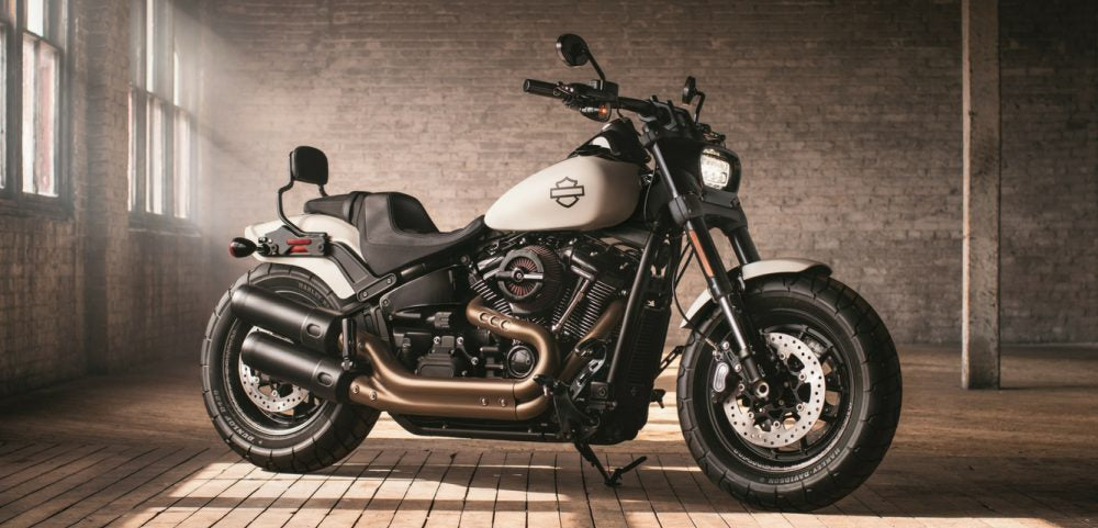 Harley Davidson motorcycle in a sunlit room with wooden floor and brick wall with Dunlop tyres fitted.