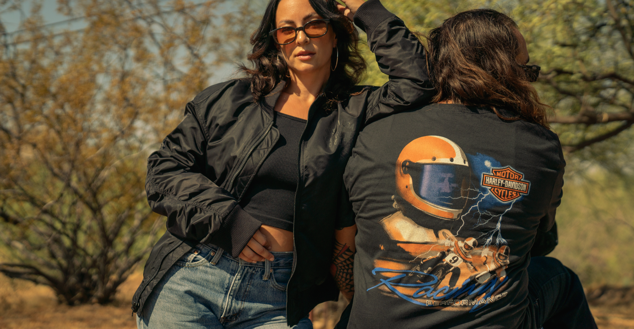 Man and a women outdoors with one adjusting the hair of the other, set against a natural background wearing Harley-Davidson.