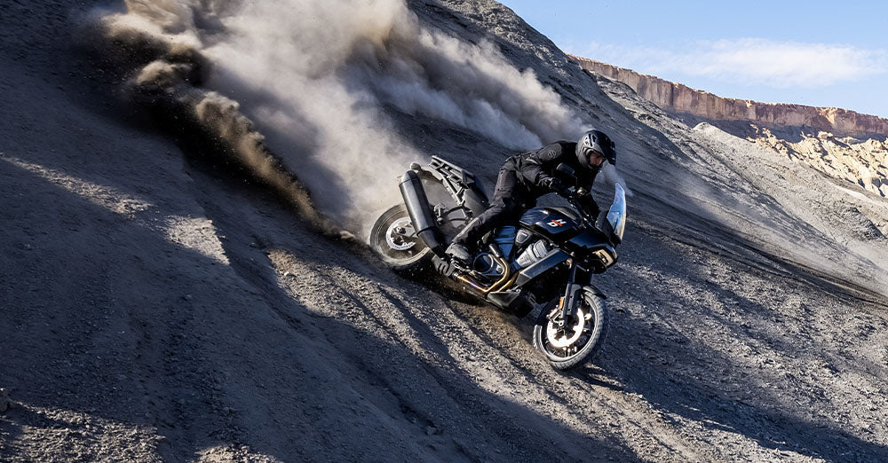 Person riding a Harley-davidson Pan America motorcycle on a dirt hill with dust in the air