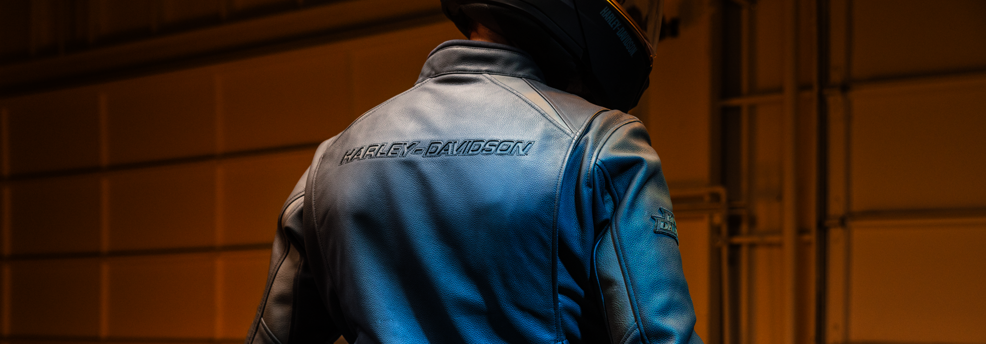 Person wearing a blue motorcycle jacket with 'Harley-Davidson' branding against a dark background.